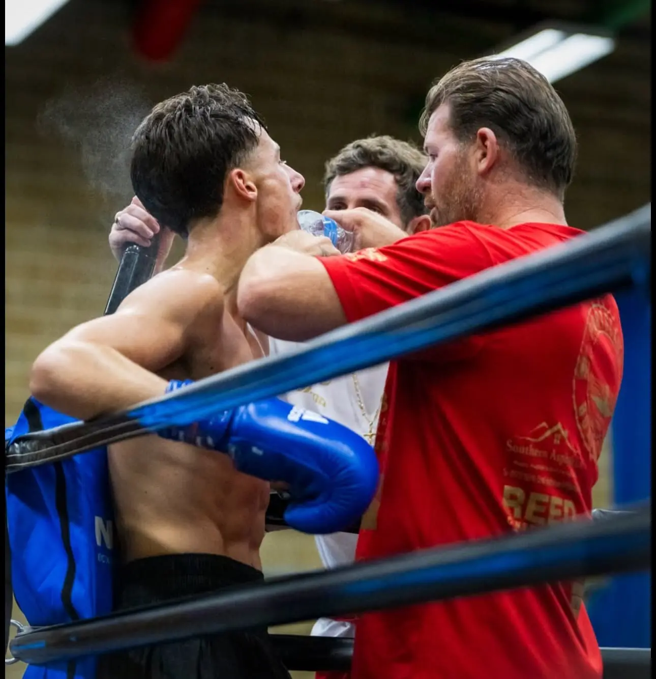 A coach giving a boxer water between rounds while leaning over the ropes