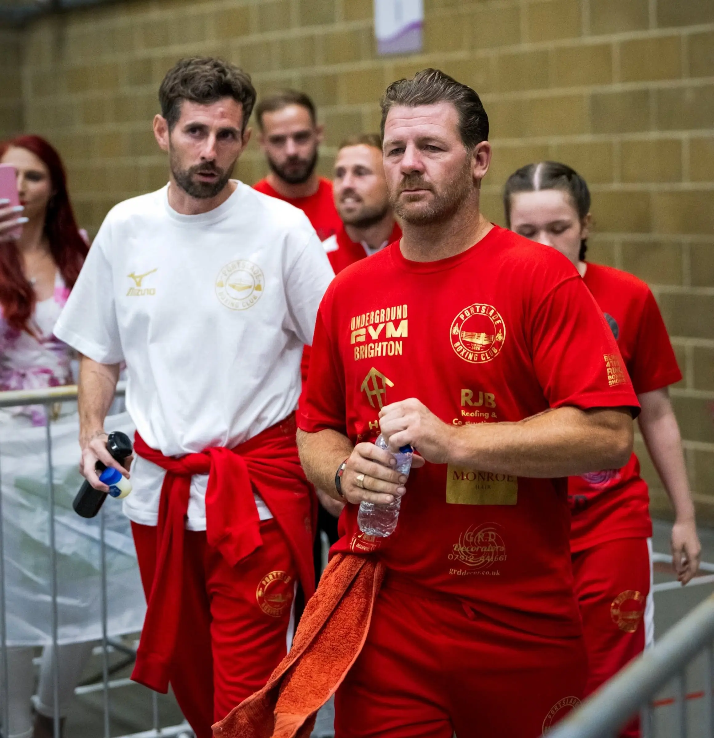 A coach in a red club T-shirt walking through the crowd at a show, with a boxer close behind